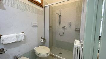 Un baño con inodoro, bidé, lavabo y una zona de ducha con mampara de vidrio.