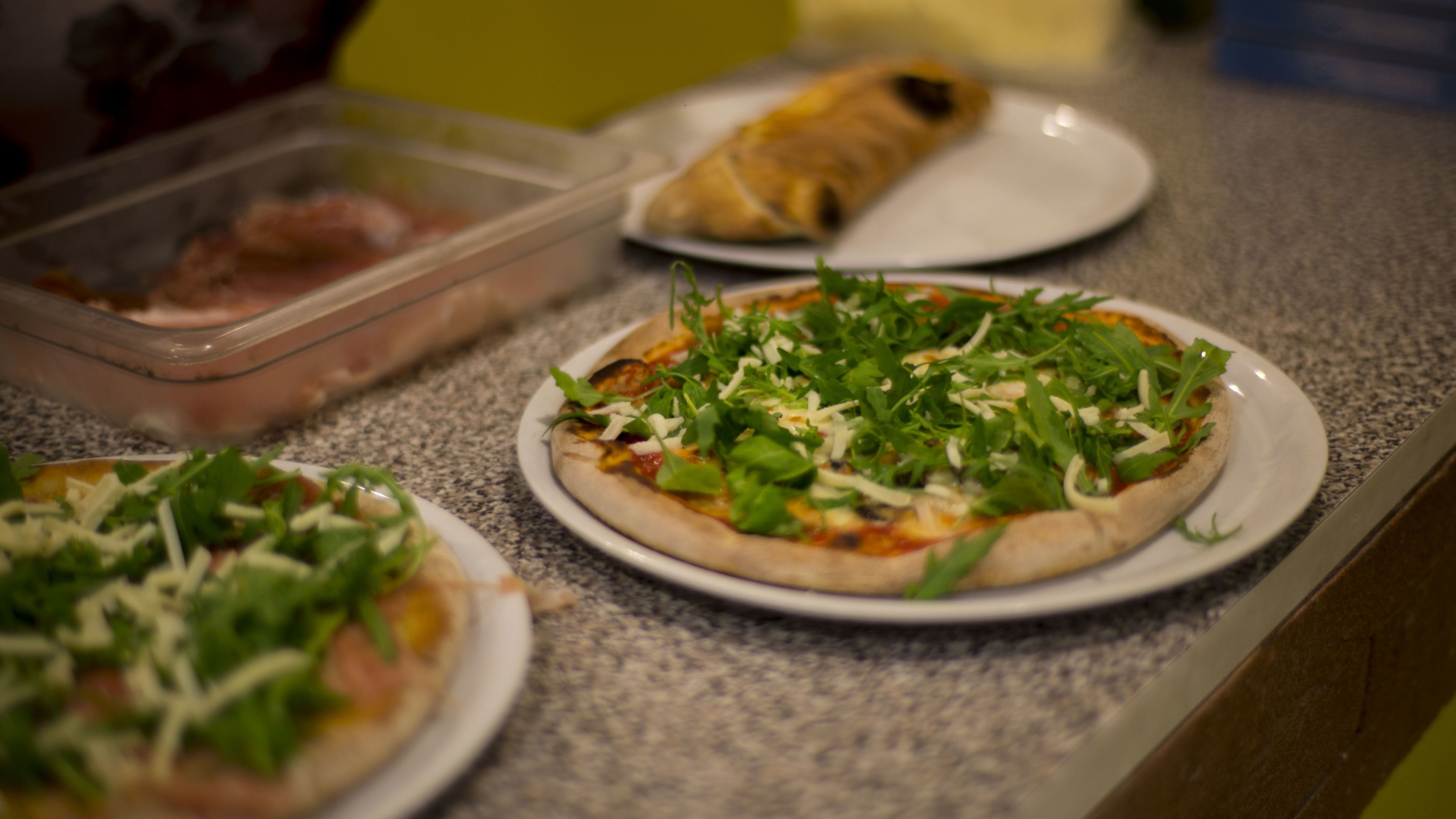 A kitchen counter with three pizzas topped with various ingredients.