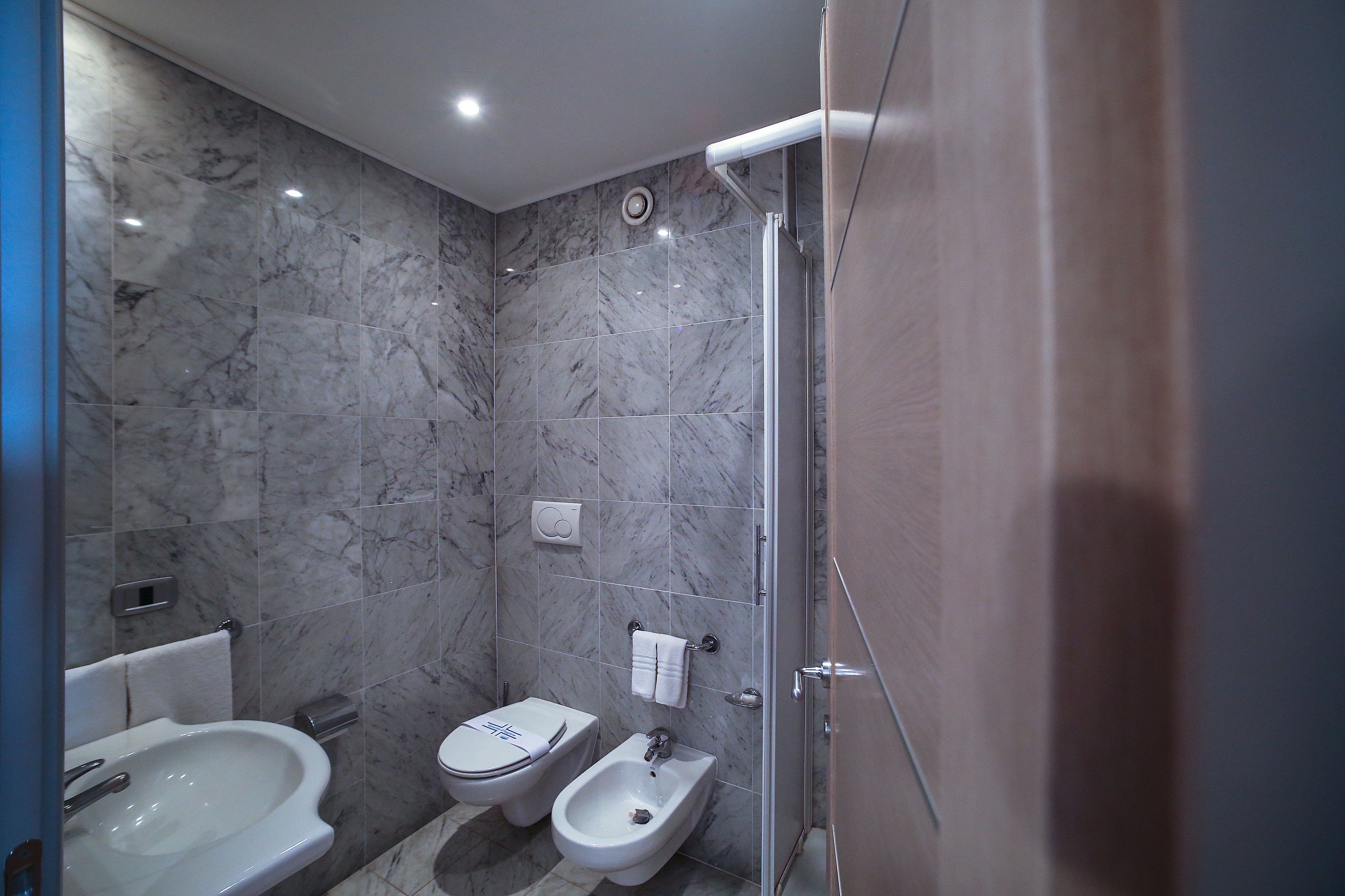A bathroom with a bidet, toilet, and sink, all with white fixtures and marble walls.