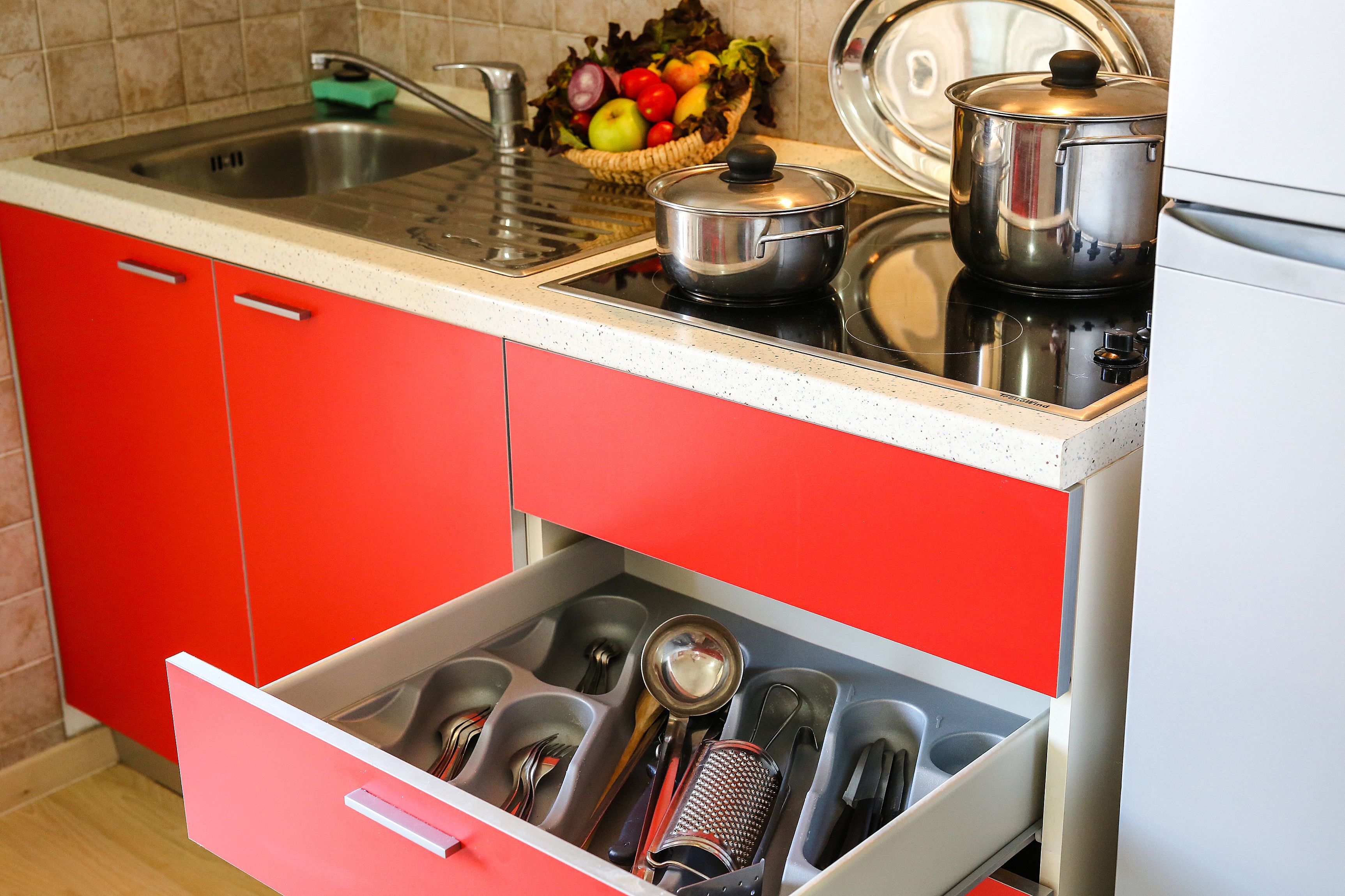 Una cucina con pensili rossi, un lavello in acciaio inossidabile e un cassetto pieno di utensili da cucina.