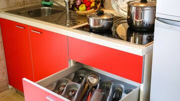 Una cucina con pensili rossi, un lavello in acciaio inossidabile e un cassetto pieno di utensili da cucina.