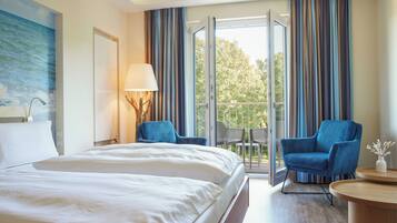 Habitación de hotel con cama, escritorio, dos sillas, lámpara y vista al exterior.