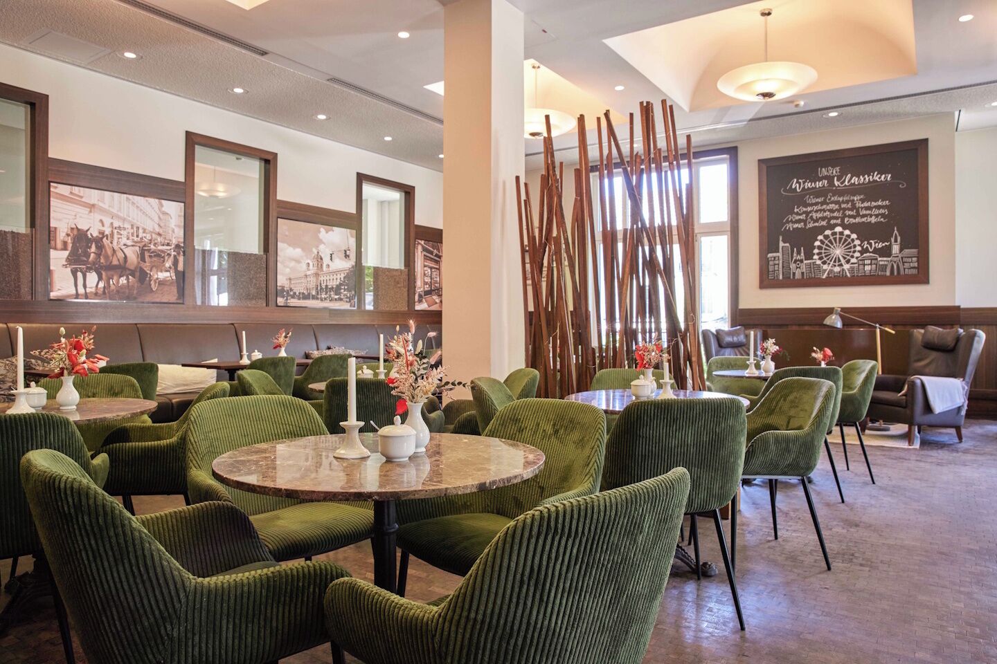 Un comedor de hotel con mesas redondas y sillas tapizadas en verde, obras de arte enmarcadas en las paredes y una estructura de madera decorativa.
