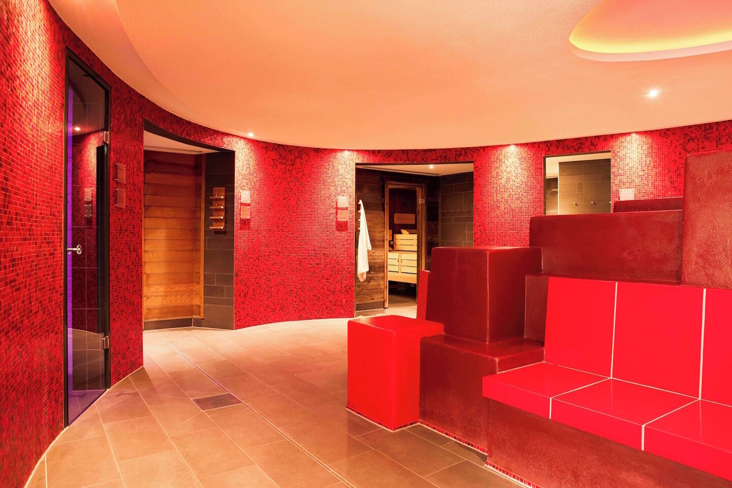 A modern interior with red-tiled walls, a curved ceiling, and a staircase with red steps.