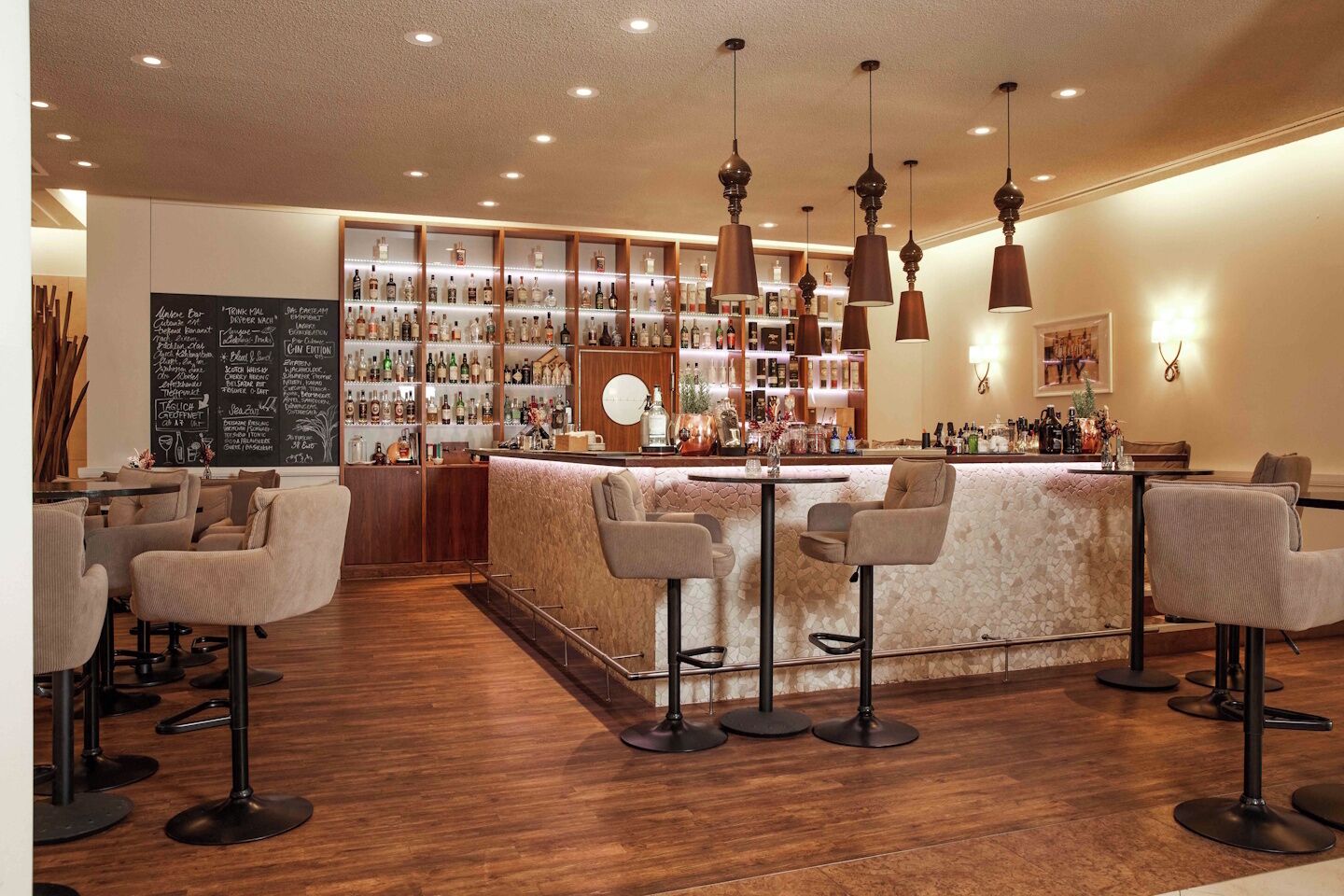 Zona de bar con barra de madera, varios taburetes y una variedad de botellas en estantes.