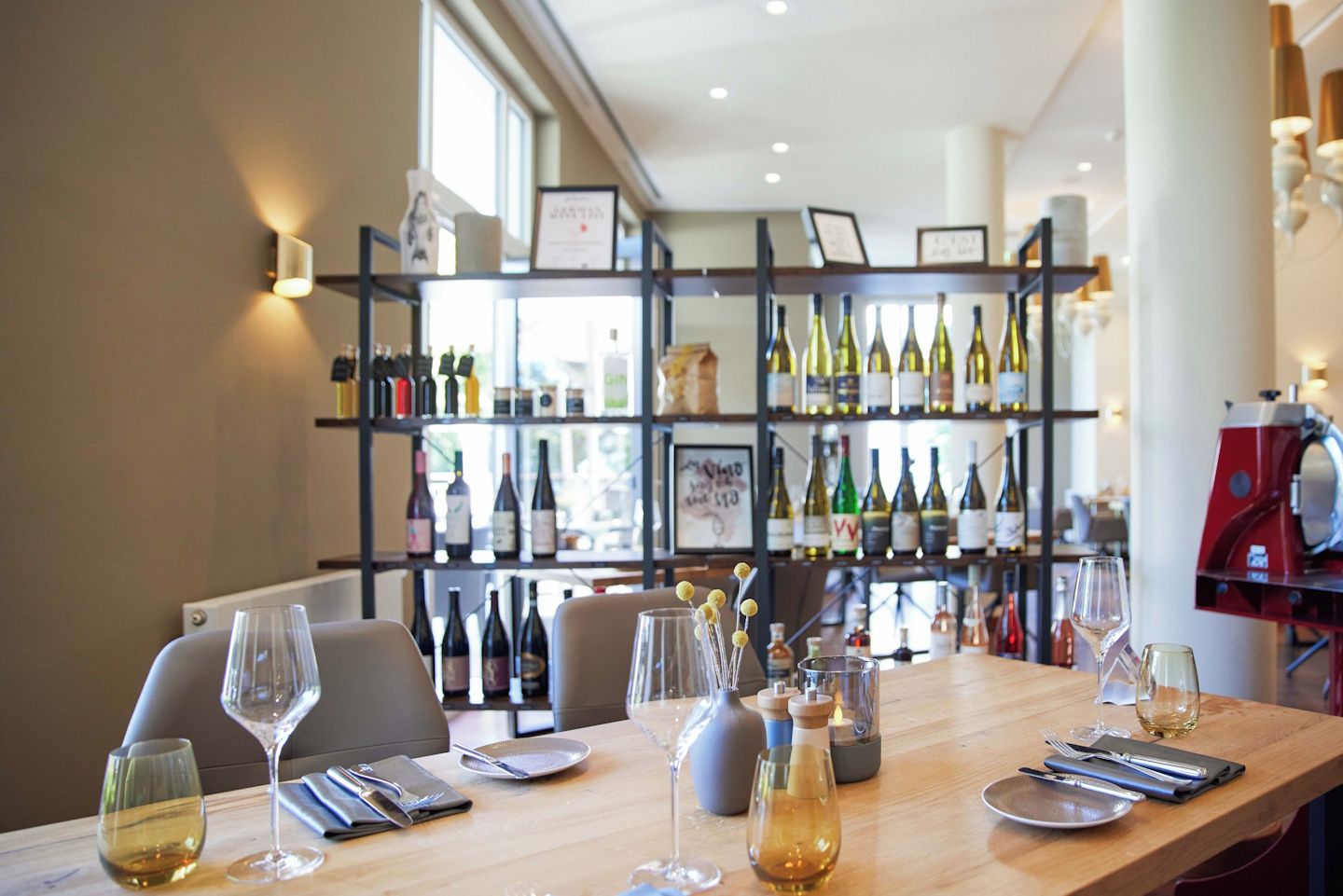 A restaurant interior with a long table set for dining, a wine rack in the background, and a coffee machine on the right.