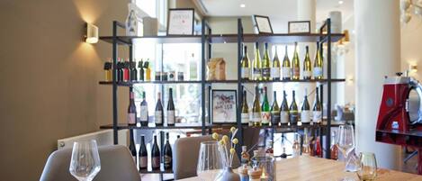 A restaurant interior with a long table set for dining, a wine rack in the background, and a coffee machine on the right.