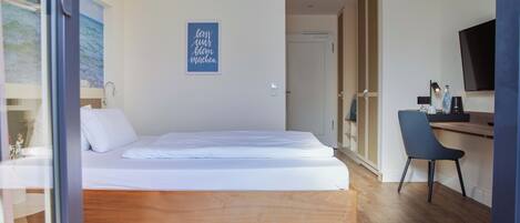 Ein modernes Schlafzimmer mit einem Holzbett, einem Schreibtisch mit Stuhl, einem Fernseher und einer Tür zu einem anderen Raum.