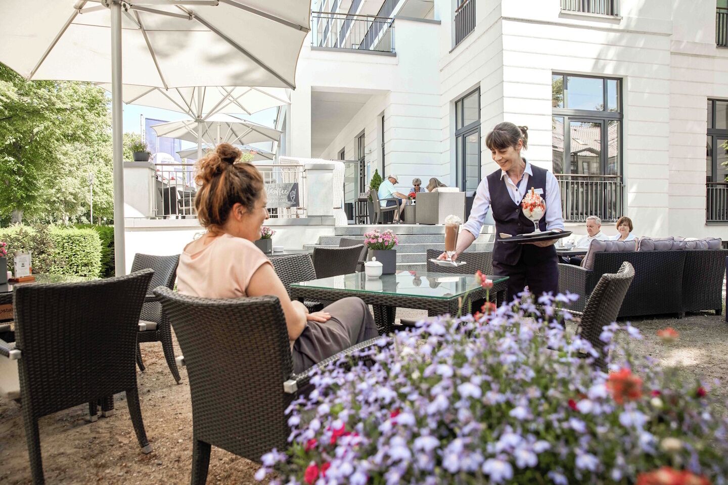 Een terras met rieten meubels en een ober die een klant bedient.