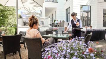 Een terras met rieten meubels en een ober die een klant bedient.