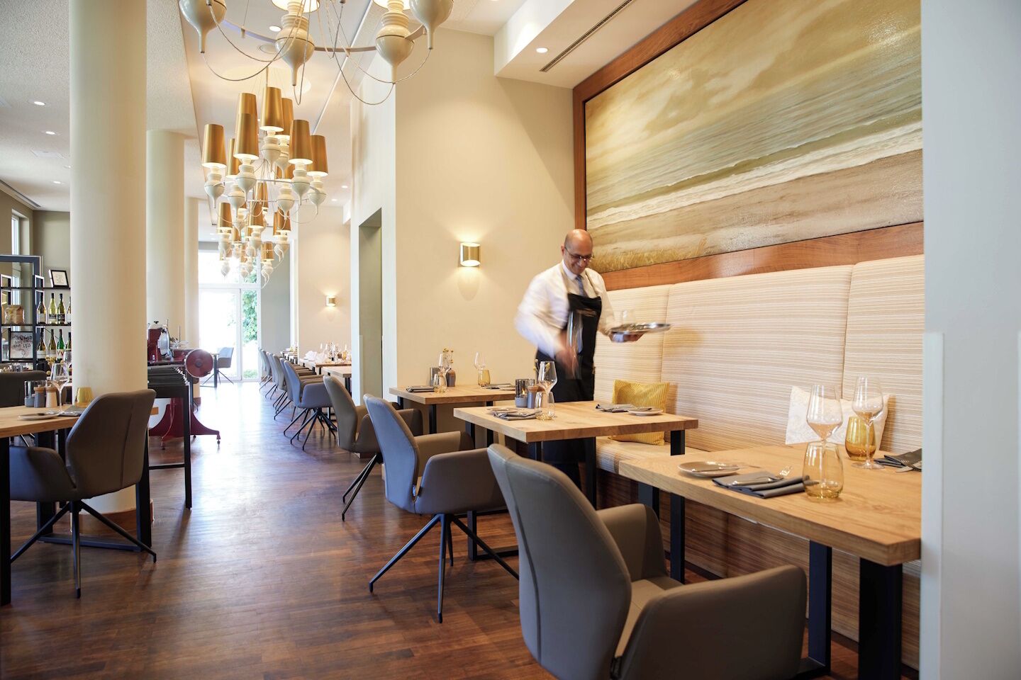 A restaurant with a long counter, modern chairs, and a waiter serving.