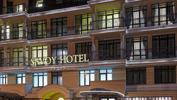 Un hotel de varios pisos con balcones y un letrero que dice 'SAVOY HOTEL'.