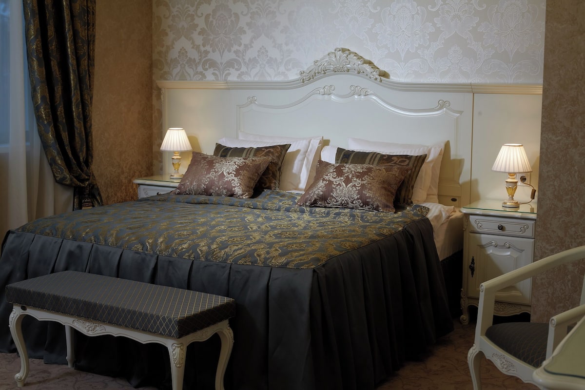 A neatly arranged bedroom with a large bed, two bedside tables with lamps, a bench, and a chair.