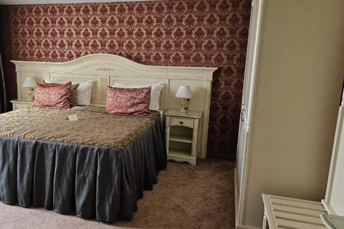 A bedroom with a large bed, two bedside tables, a chair, and a patterned wallpaper.