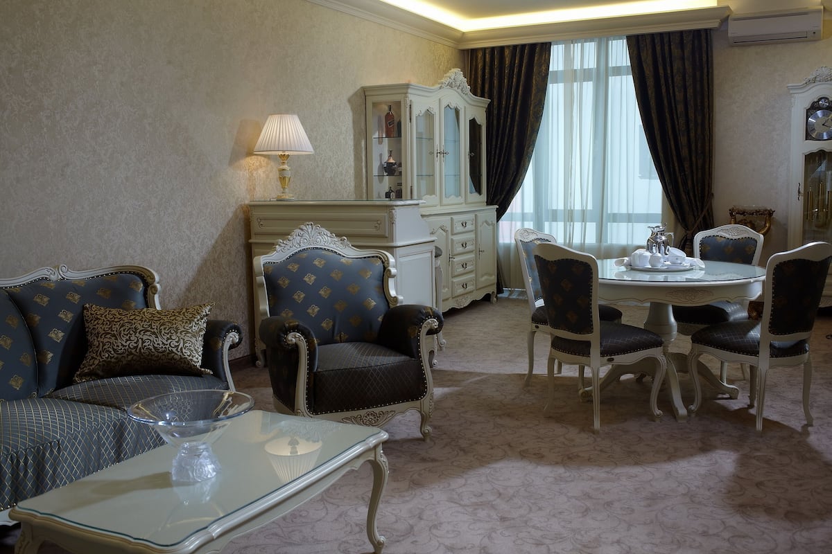 A room with a sofa, armchairs, a dining table with chairs, a cabinet, and a lamp.