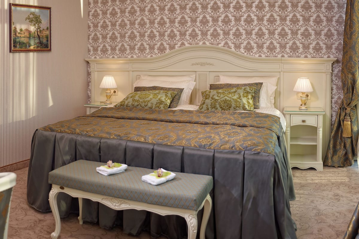 A neatly arranged bedroom with a large bed, two bedside tables with lamps, a bench, and a chair.