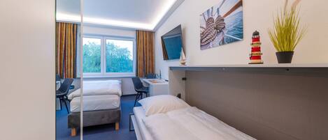 A hotel room with two beds, a desk, a chair, a TV, and a window with curtains.