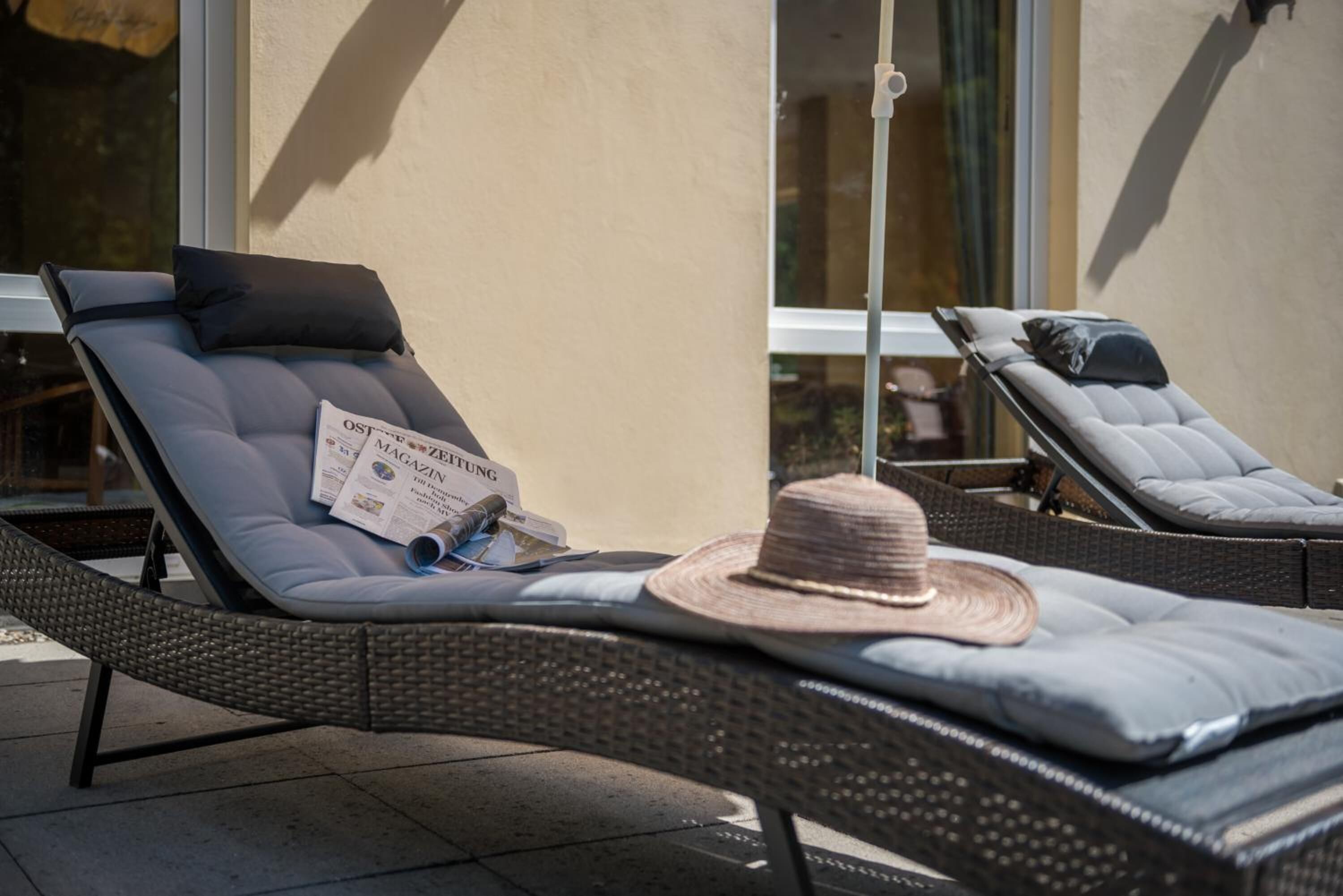 Dos sillones con cojines, un periódico y un sombrero de paja sobre uno de ellos.