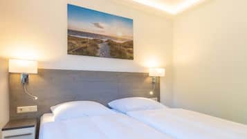 Habitación de hotel con cabecera de madera, dos lámparas de noche, una mesita de noche con cajón y un cuadro con una escena de playa sobre la cama.
