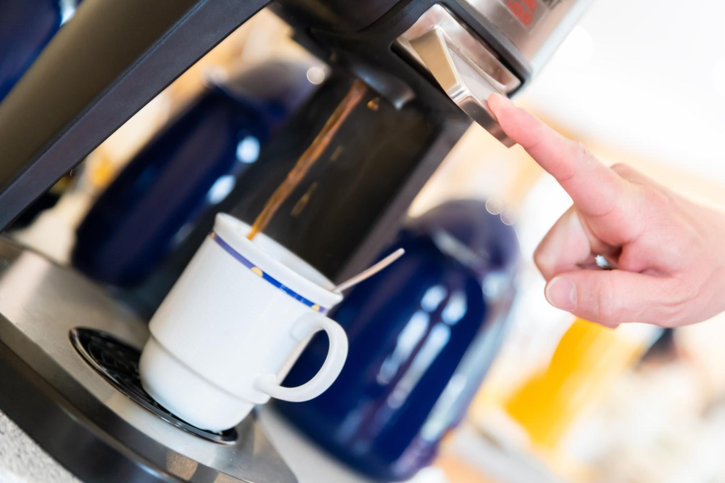 A hand placing a cup under a coffee machine.