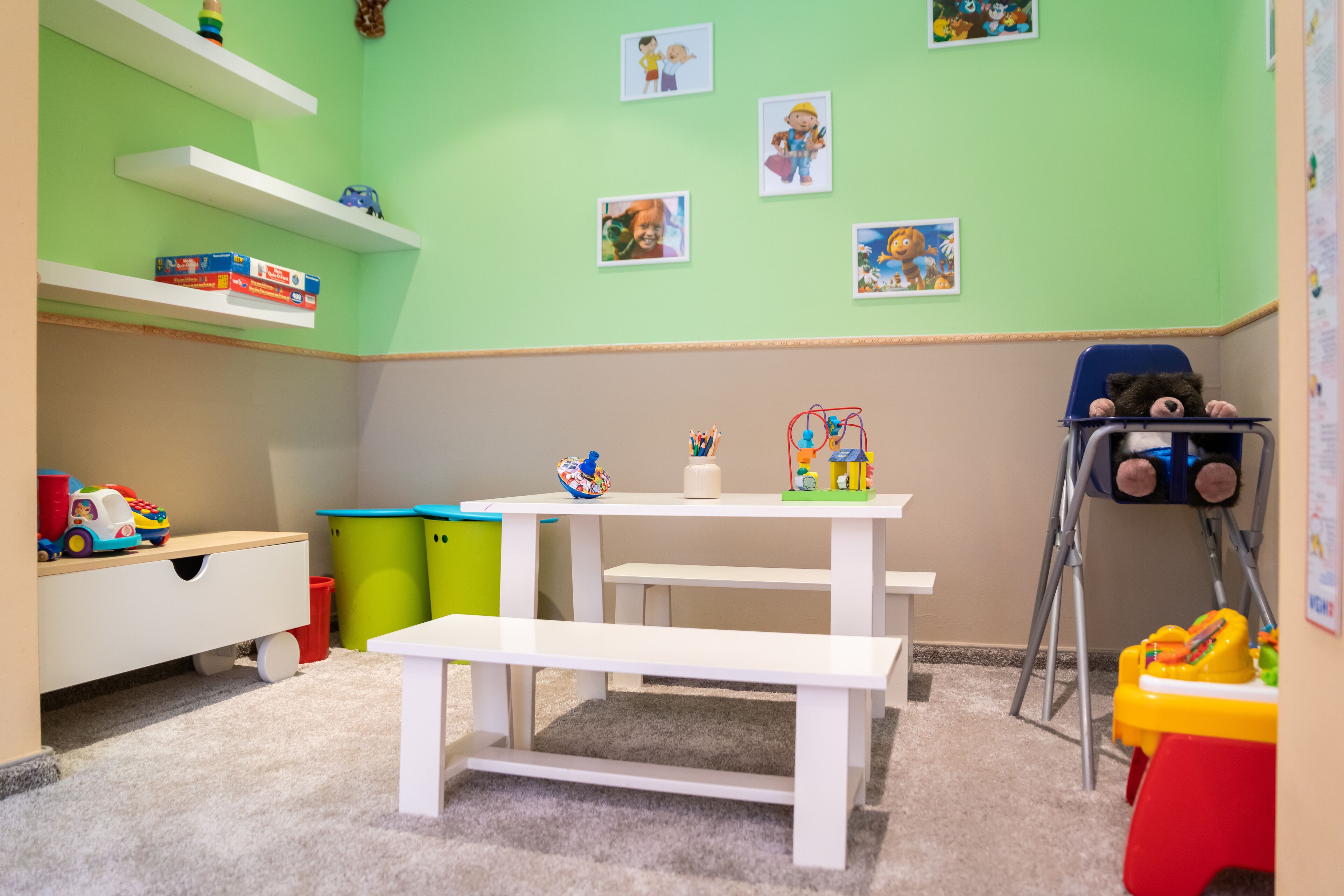 A children's playroom with a white table, shelves, and toys.