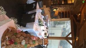 Un espace repas avec une longue table dressée pour un repas, agrémenté d’un centre de table décoratif composé d’aliments et de fleurs.