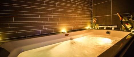 A modern spa room with a large bathtub, a brick wall, and a bottle of champagne.