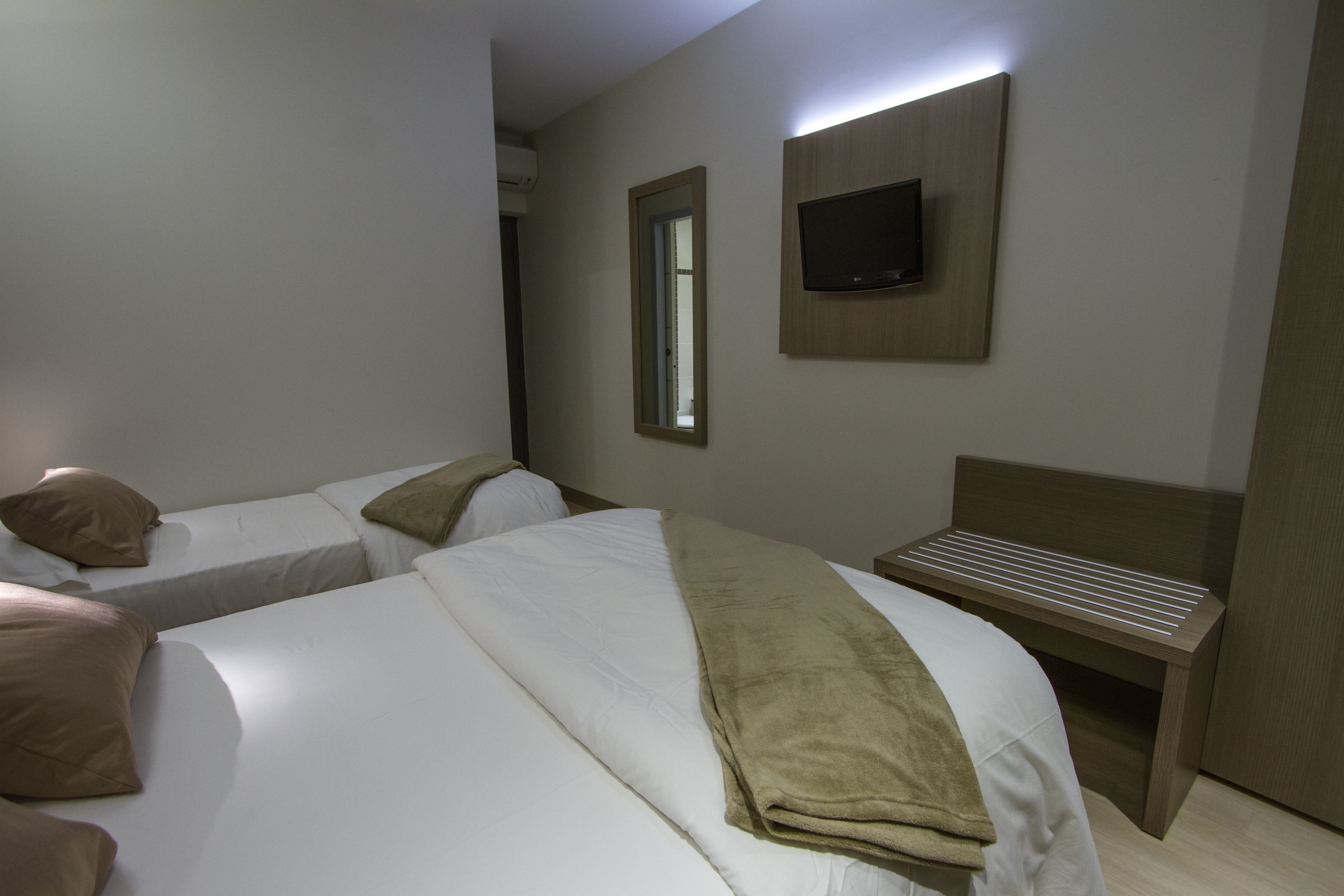 A hotel room with two beds, a TV mounted on the wall, and a bench.