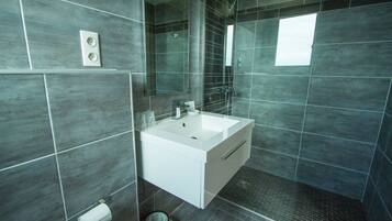 A modern bathroom with a white sink, dark tiles, a mirror, and a shower area.