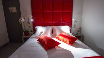 A hotel room with a red headboard, white bedding, and a small bedside table with a plant and a phone.