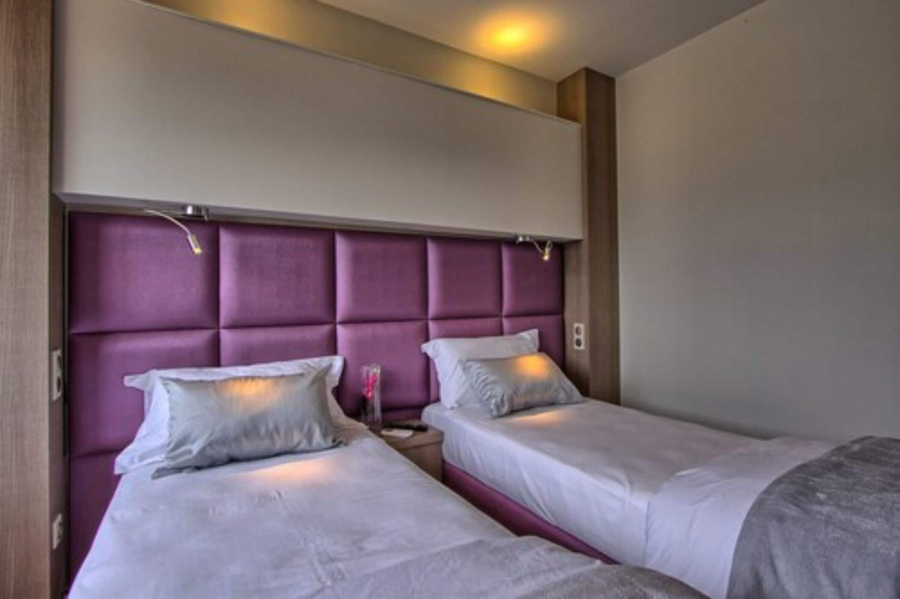 A hotel room with two beds, each with white bedding and a purple headboard.