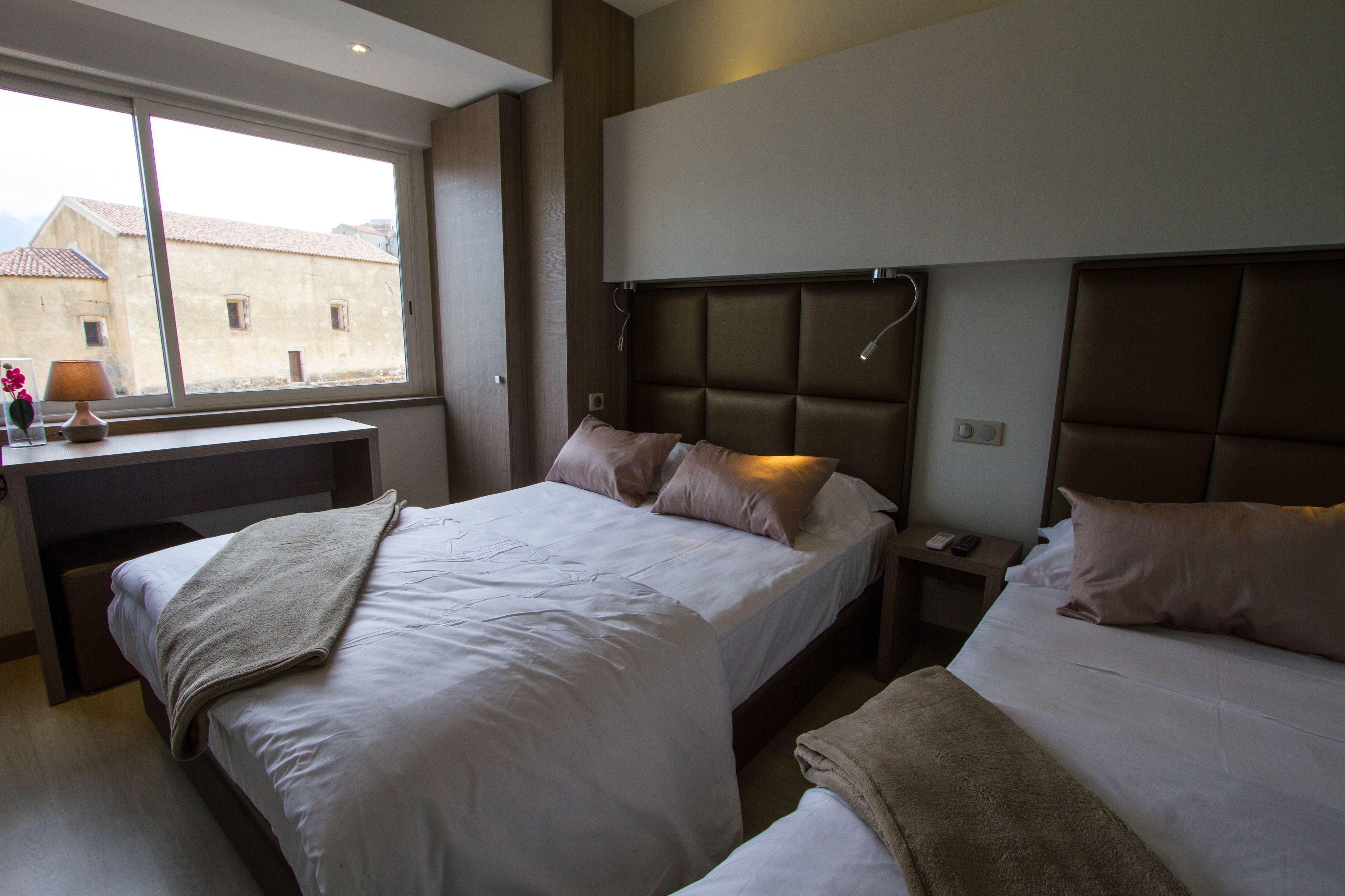 Habitación de hotel con dos camas, un escritorio y una ventana con vista a edificios.