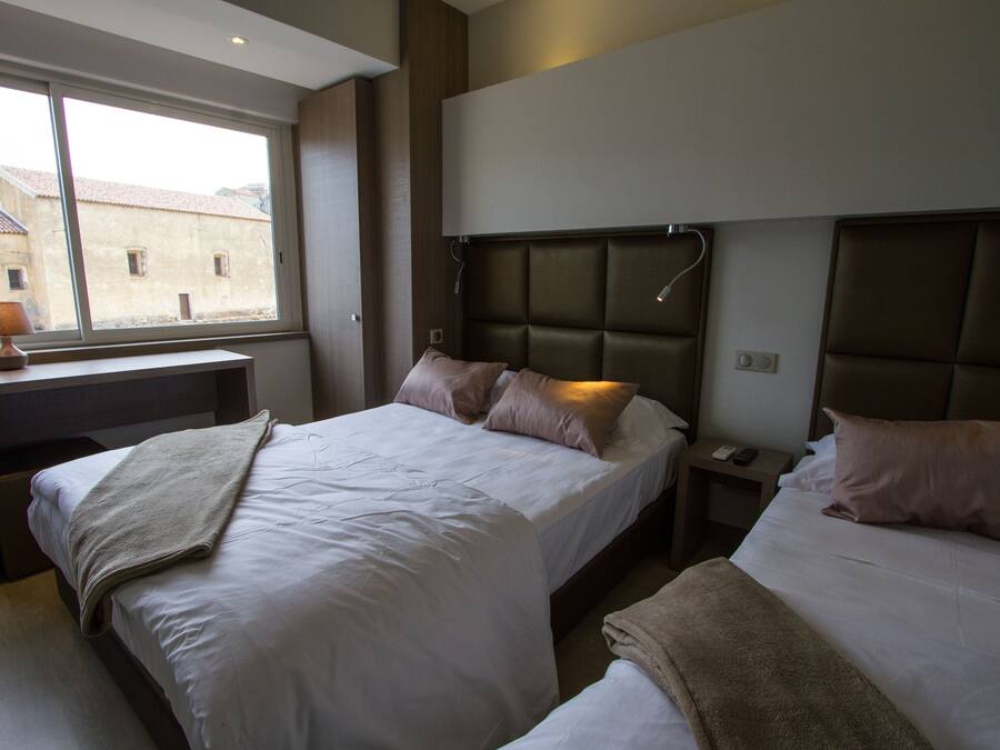 Habitación de hotel con dos camas, un escritorio y una ventana con vista a edificios.