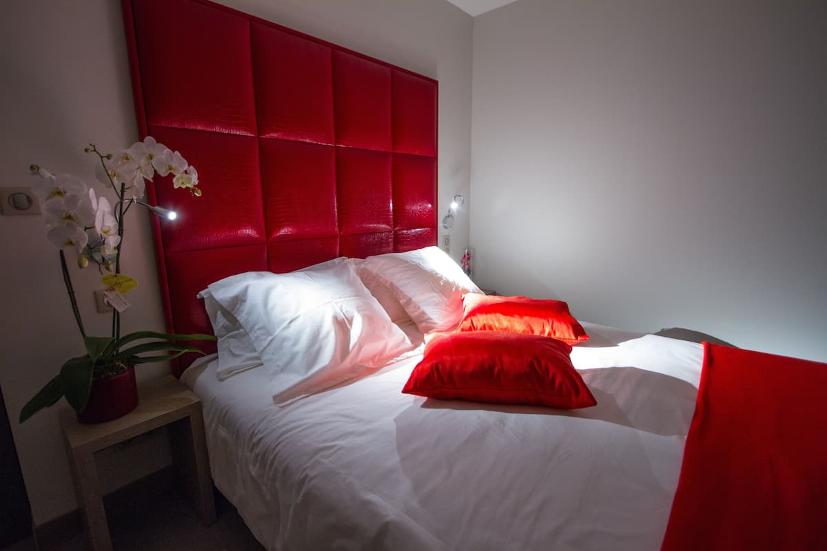 A neatly made bed with white and red bedding, a red headboard, and a bedside table with a potted plant.