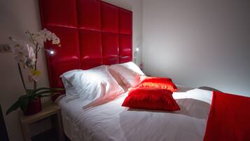 A neatly made bed with white and red bedding, a red headboard, and a bedside table with a potted plant.
