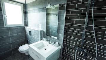 Ein modernes Badezimmer mit einer Duschkabine, einem weißen Waschbecken und einer Toilette.
