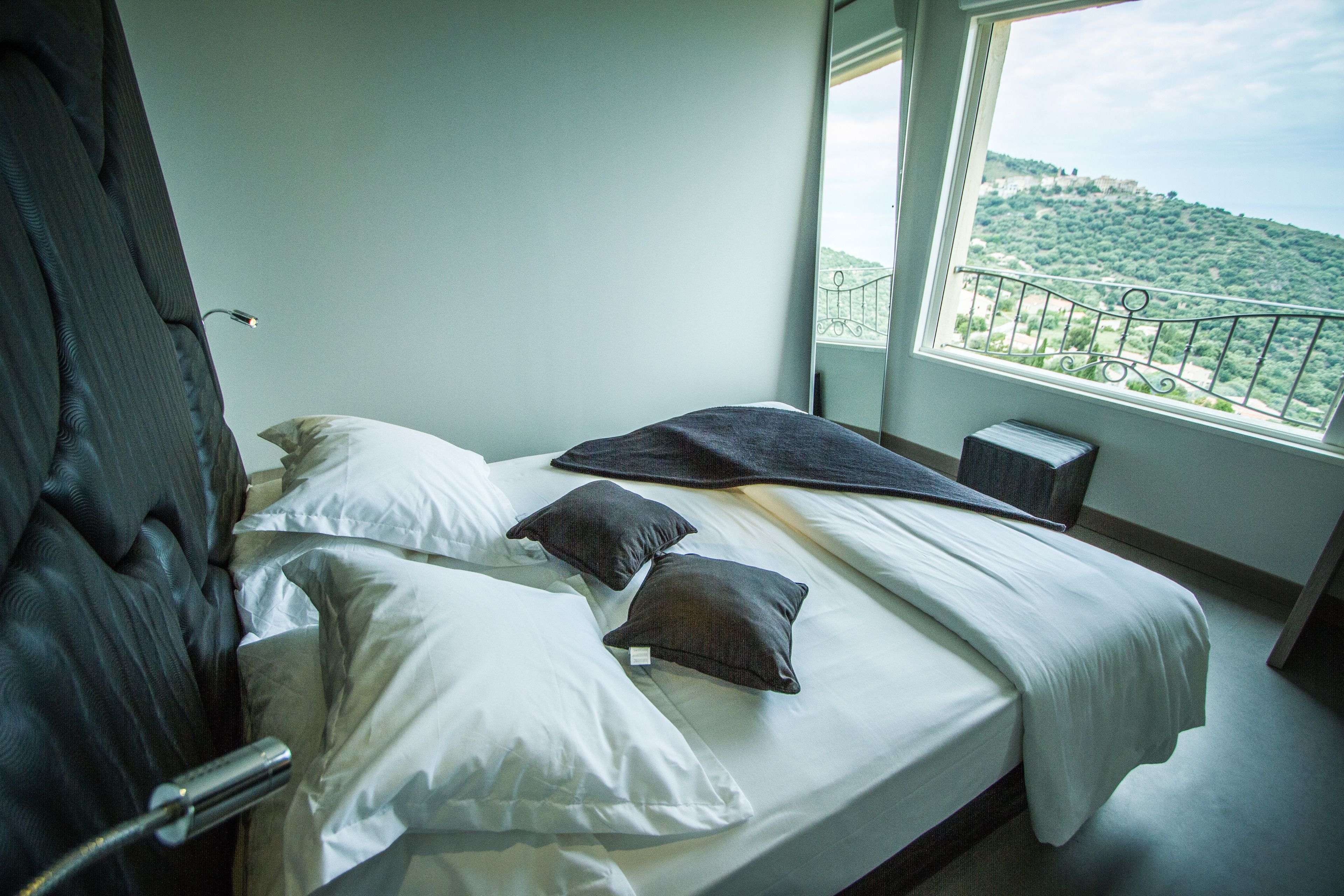 Habitación de hotel con cama, almohadas, mesita de noche y vistas a un paisaje verde por la ventana.