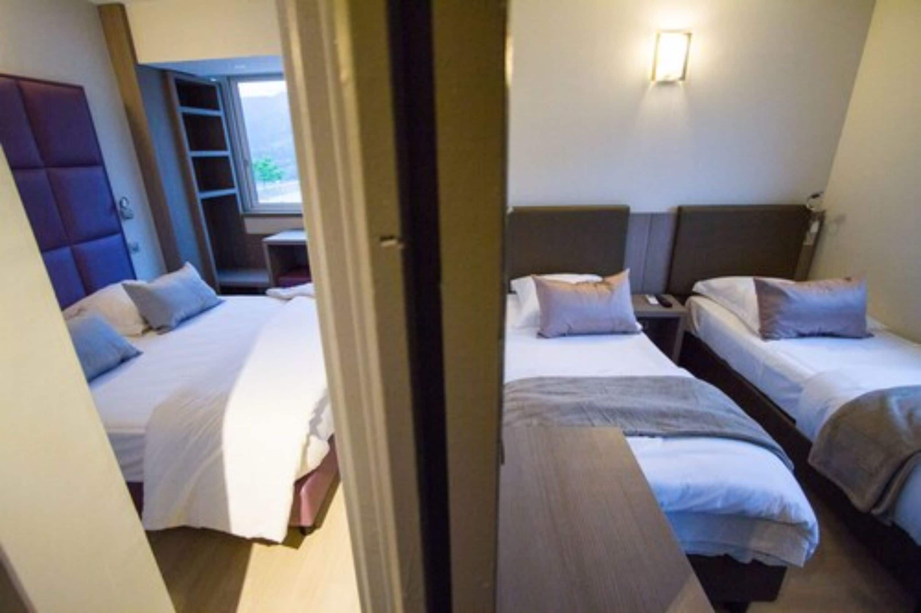 Ein Hotelzimmer mit zwei Betten, einem Kleiderschrank, einem kleinen Tisch und einem Fenster mit Blick.