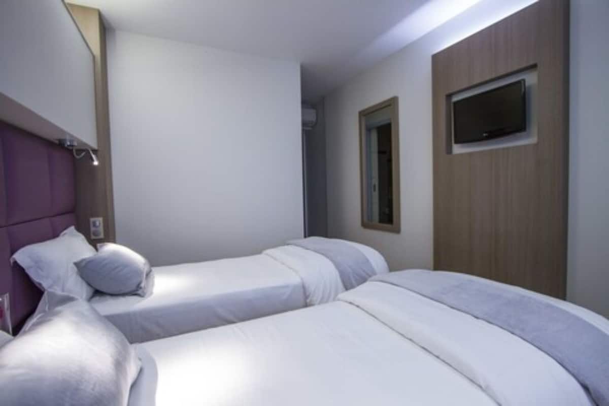 A hotel room with two single beds, a wooden headboard, a mounted TV, and a window with a view.