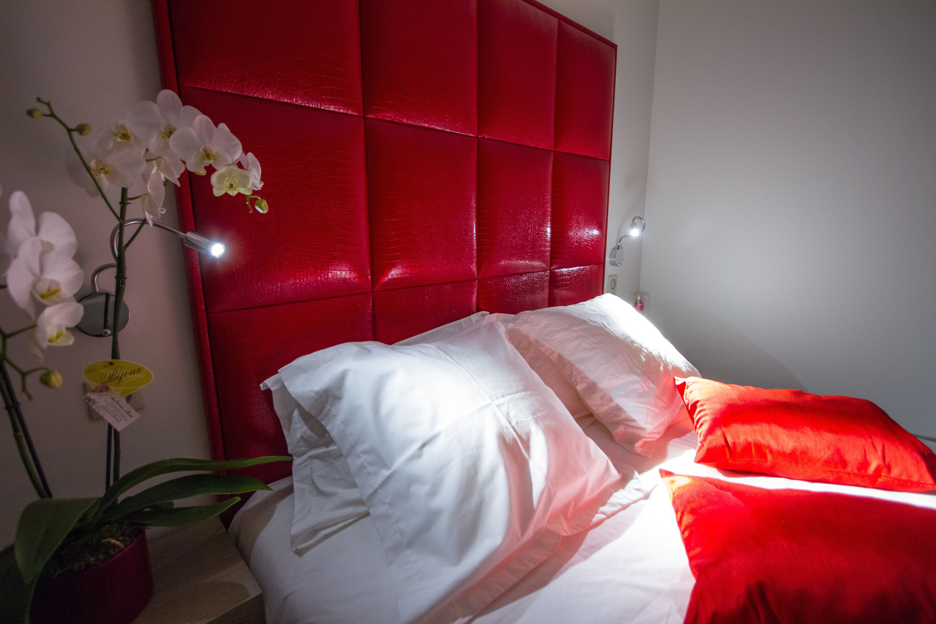 A bedroom with a red headboard, white bedding, and a potted orchid.