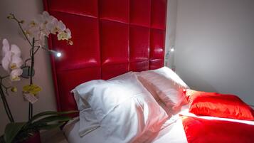 A bedroom with a red headboard, white bedding, and a potted orchid.