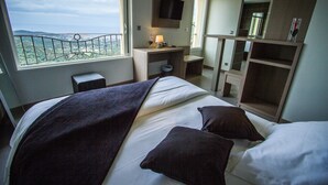 Une chambre d’hôtel avec un lit, un bureau, une télévision et un balcon offrant une vue.