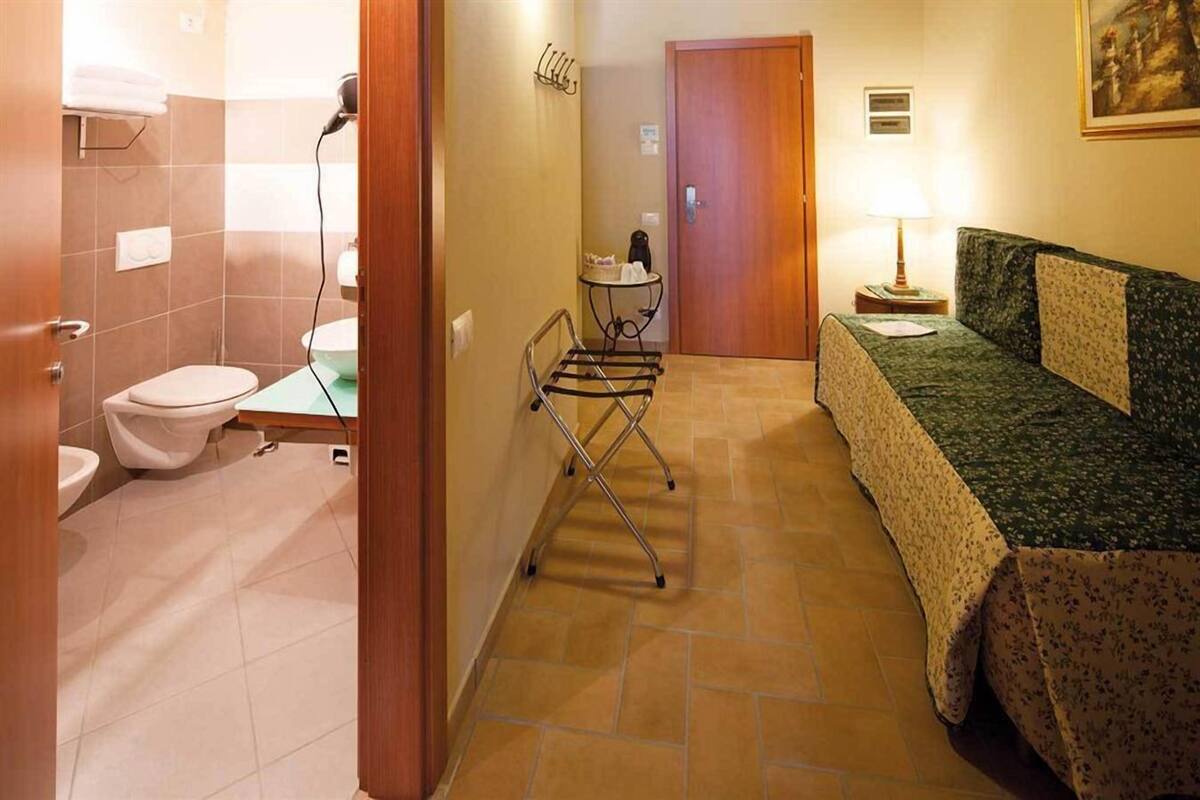 A bathroom with a toilet, sink, and a towel rack. There is a small table with a lamp and a painting on the wall.