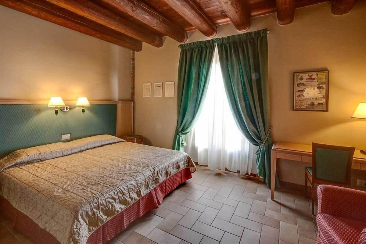 A hotel room with a bed, a desk, a chair, and a window with curtains.