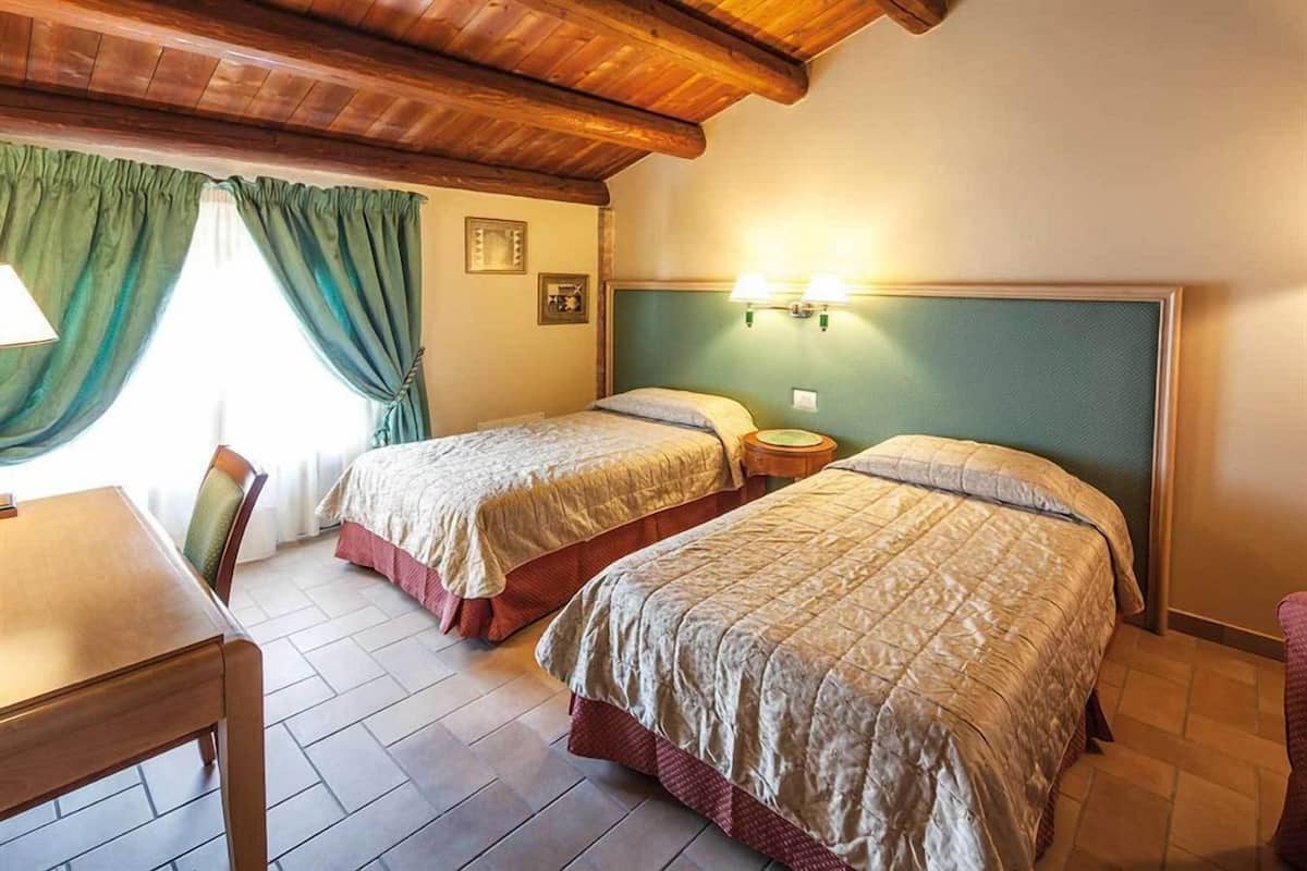 A room with two beds, a wooden table, and a window with curtains.