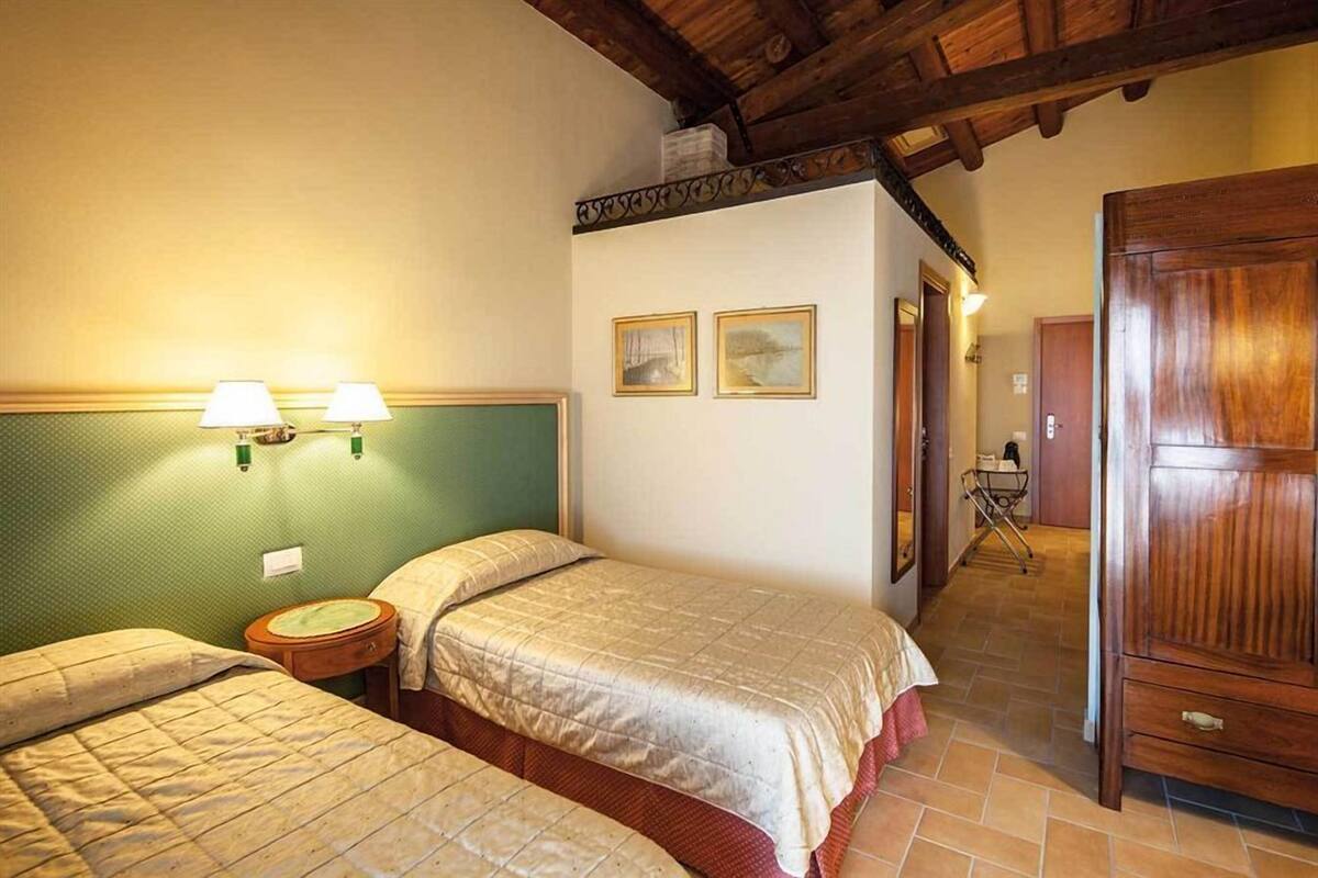 A room with two beds, a wooden wardrobe, and a green wall with two framed pictures.
