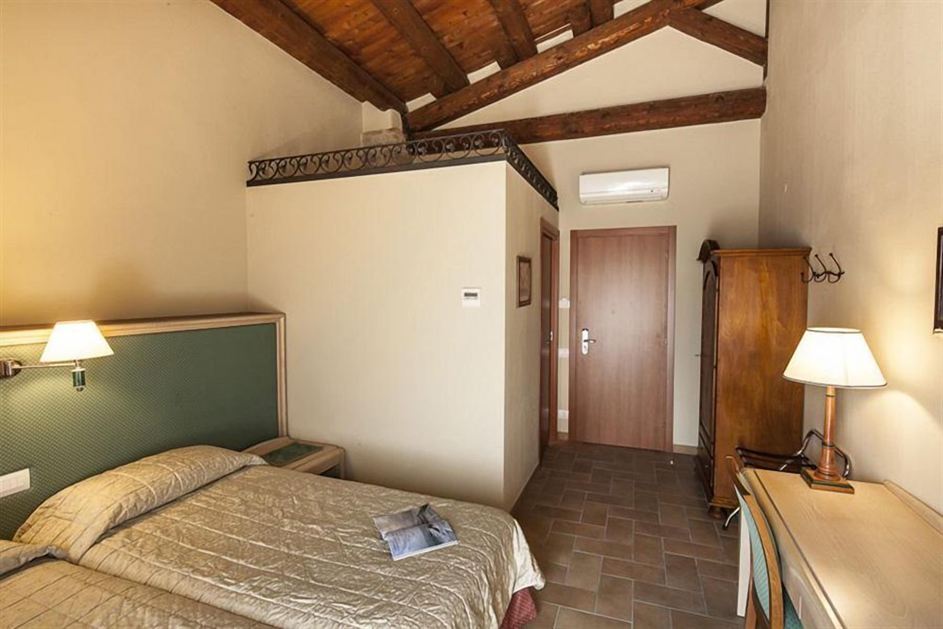 Ein Schlafzimmer mit einem Bett, einem Holzschrank, einem Schreibtisch mit Lampe und einer Tür zu einem anderen Raum.