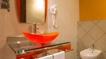 A modern bathroom with a glass sink, a large mirror, a hairdryer, a bidet, and a towel rack.