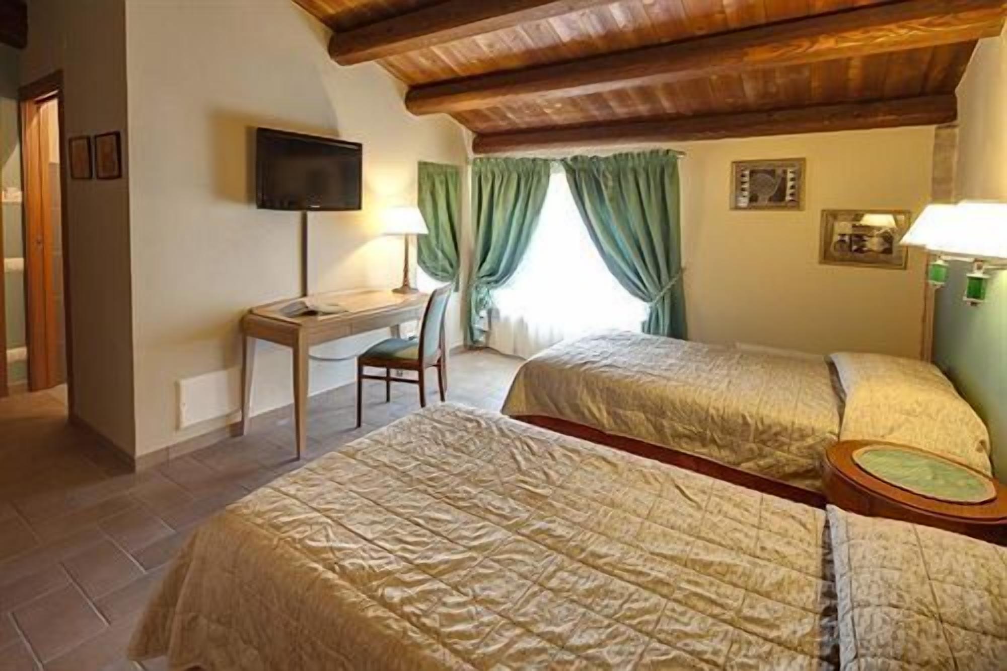A hotel room with two beds, a desk with a chair, a television, and a window with curtains.