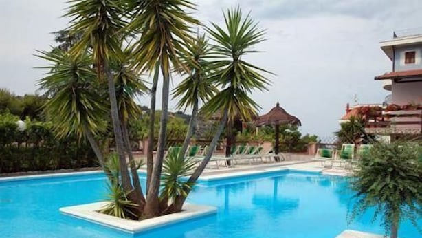 Ein Swimmingpool, umgeben von Palmen und Liegestühlen, mit einem Gebäude im Hintergrund.